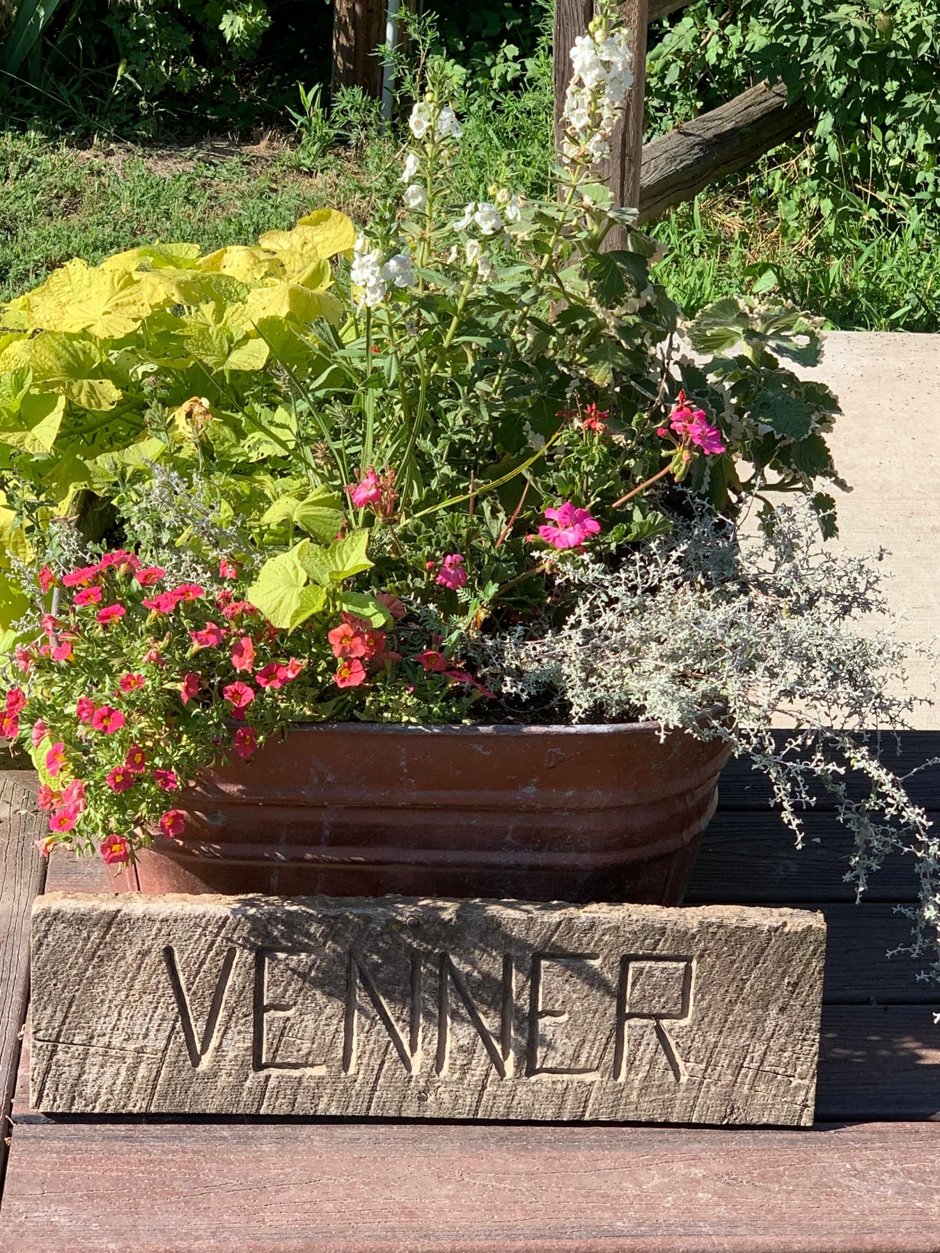 A wooden planter box carved with the name VENNER, spilling over with flowers