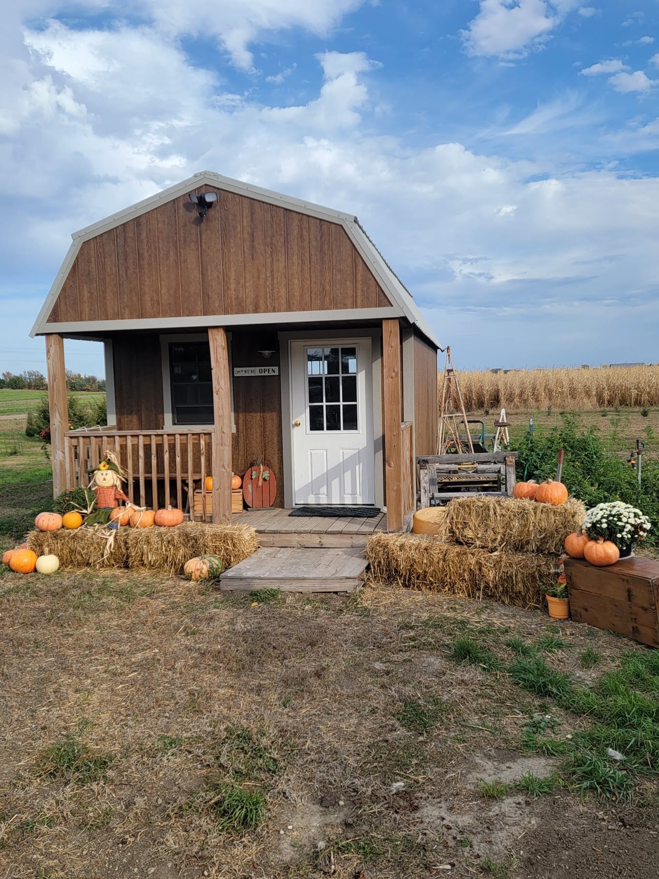 The Venner Farm stand, a small wooden barn with a porch, hay bales and pumpkins out front